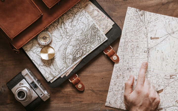 Top 10 Travelgoals 2024 - World map hand shows something on this map. A compass and a travel bag are also included