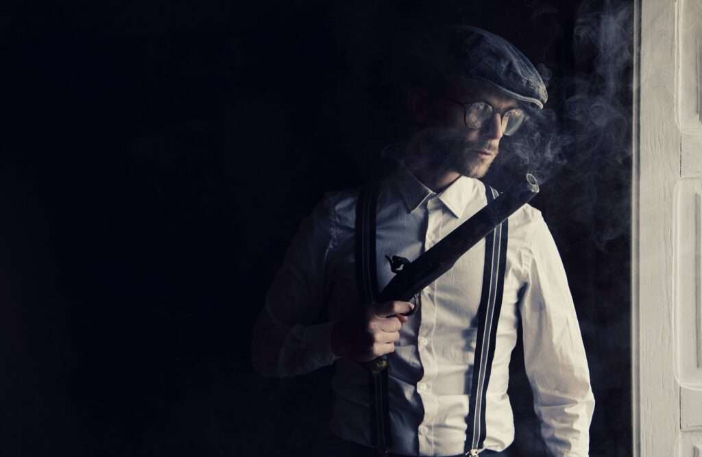 Dont vacation in England - oldschool dressed man with gun and silencer where smoke comes out. Picture kept dark