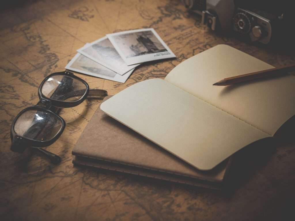 Top 10 Tips work and travel - Table with world map as background on which glasses, a pen and a notebook lie