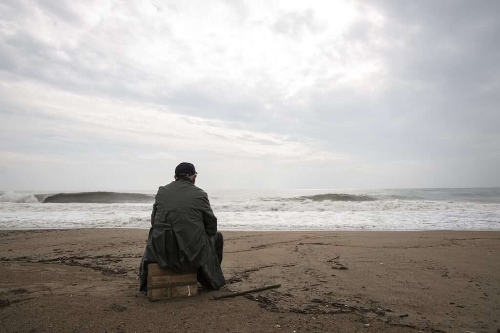 Dont vacation in England - Man sits on a suitcase in front of the sea on the beach and is depressed